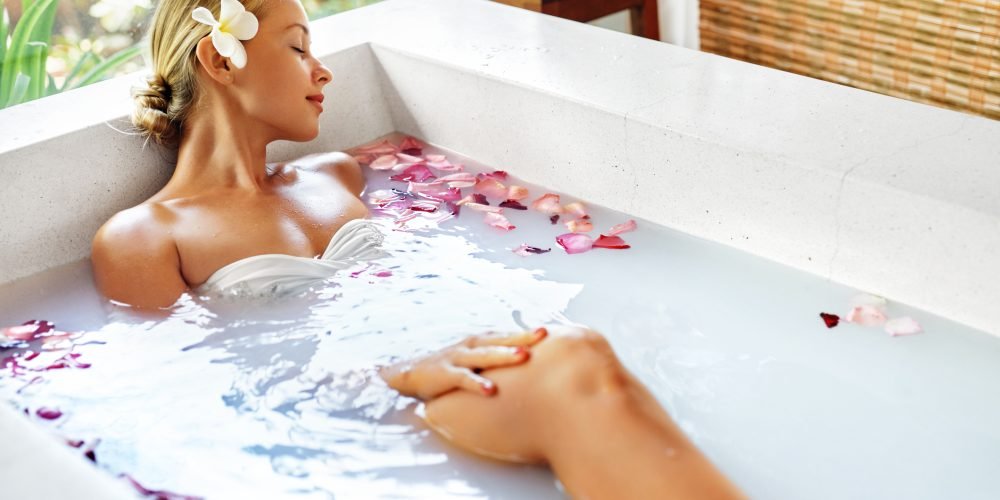 Young woman in the bathroom with flower petals and milk bath| The Sublime Woman