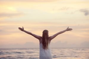 Happy woman standing in front of the water listen to your heart and soul | The Sublime Woman