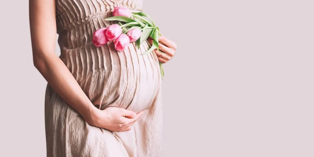 Pregnant woman holding her belly with flowers — symbol of pregnancy and spiritual meaning of miscarriage.